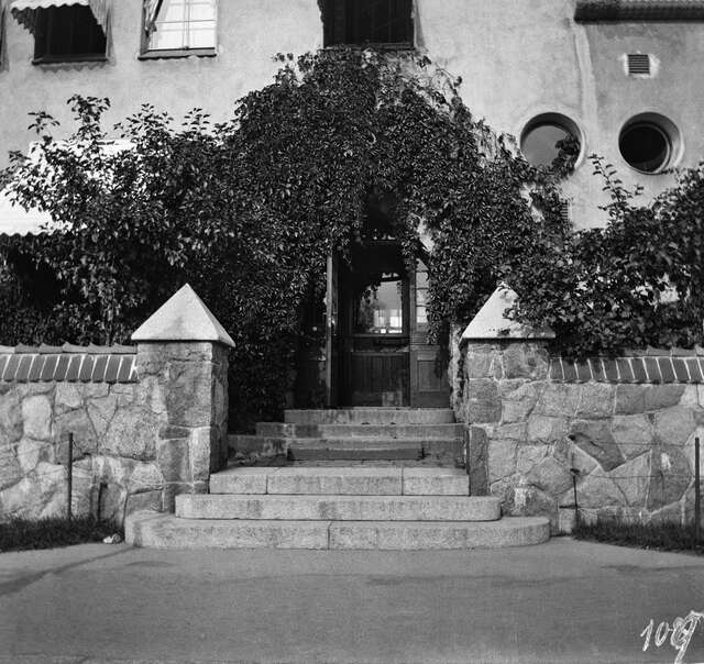 Black and white picture of the entrance with a. plant growing above the door.
