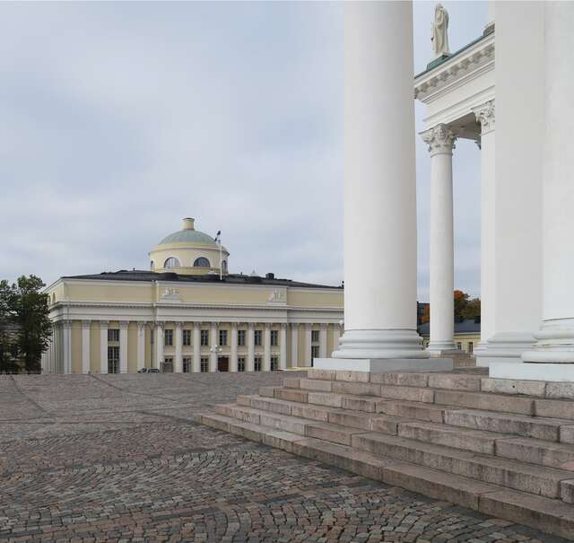 Yellow building with a green cupola and white decorative columns at the entrance and beams at the sides.