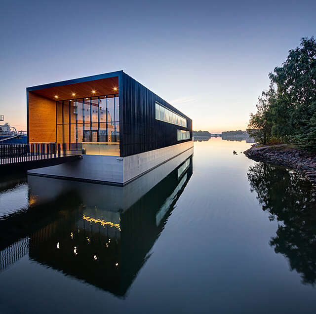 Horizontal building on the sea with black metal sheet walls and glass façade