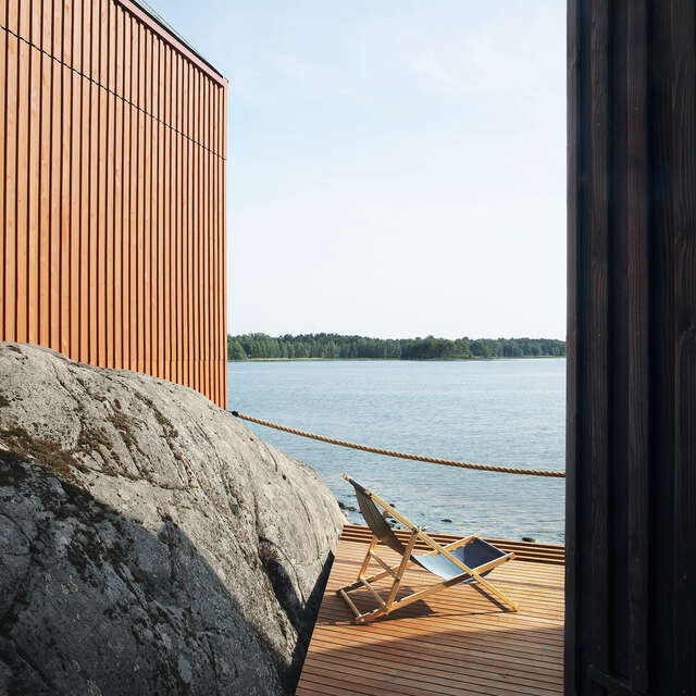 A wooden deck with a chair and a orange wooden wall on top of a rock next to the deck.