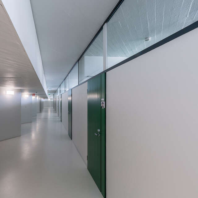 Bare white hallway with green doors on the right side.