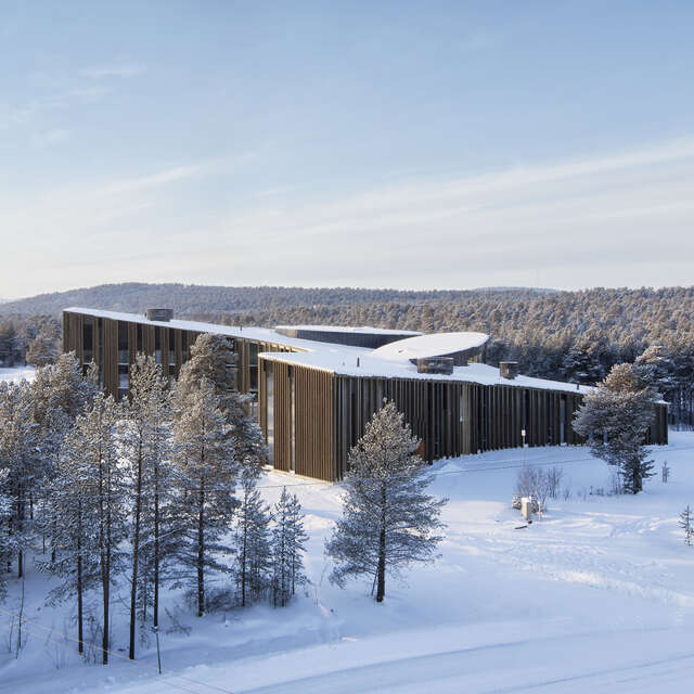 A building in a snowy landscape surrounded by trees in a bright blue light.
