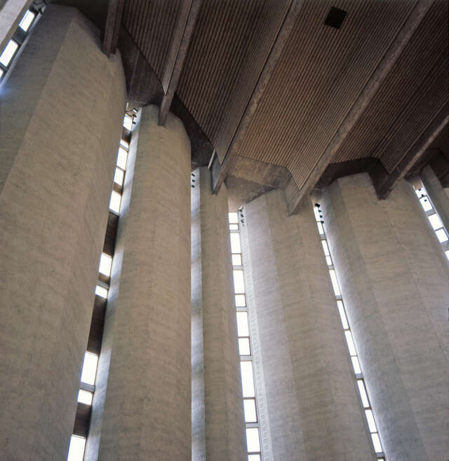 Church interior with concrete walls and ceiling with wooden beams covering most of the concrete.