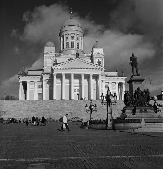 A statue of Alexander II in the middle of a square in front of a white cathedral