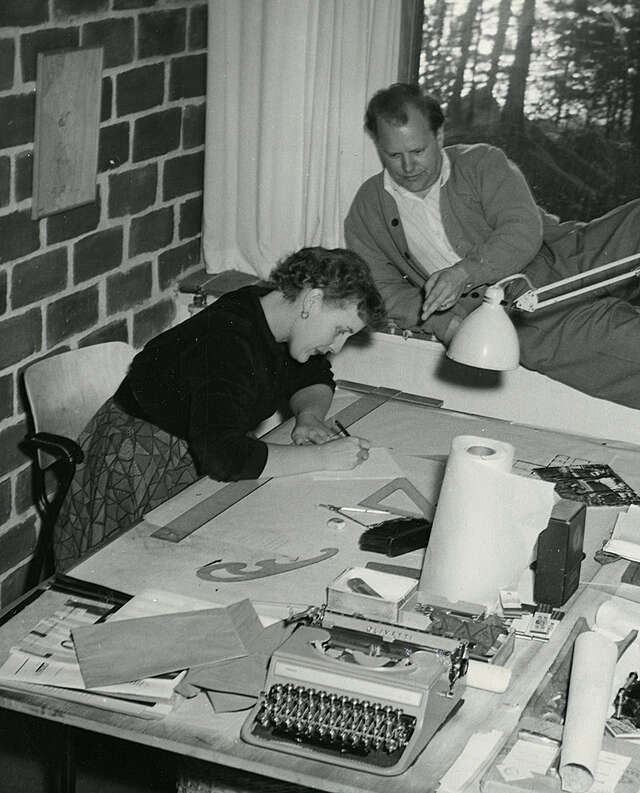 old black and white picture of a woman and man. The woman is drawing and the man looks at her.
