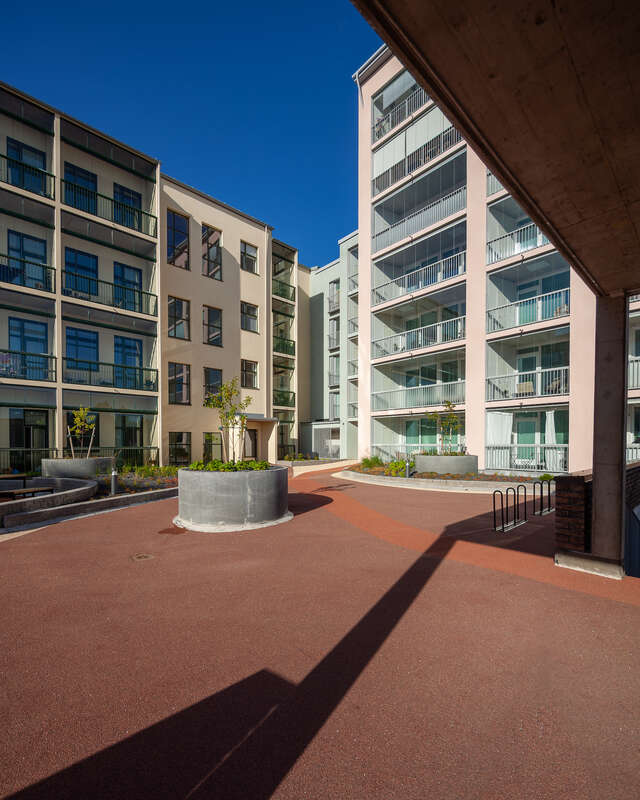 Two apartment buildings with a flat area in front of them, made of a red substance.