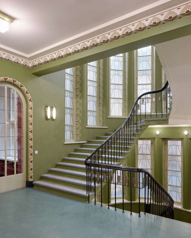 A stairwell in an old building. Green walls and thin windows surround the staircase.