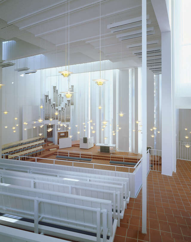 Spacious and white church interior with a view of the altar with tens of lamps hanging at different heights.