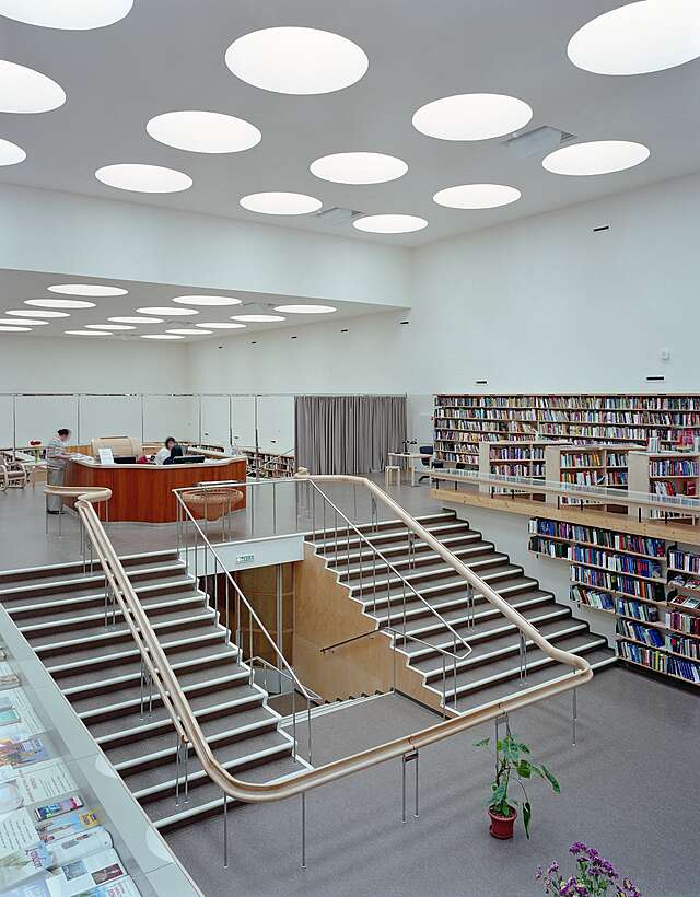 Wide stairs connecting two library levels with a curvy railing in the middle of them.
