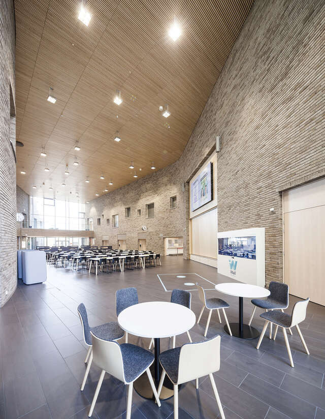 Canteen with grey-brick walls, a wooden ceiling and light furniture with blue textiles.