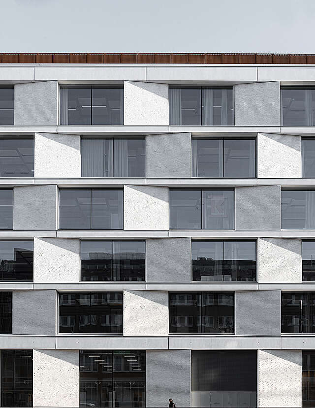 Facade detail with tilted panes of white brick and windows