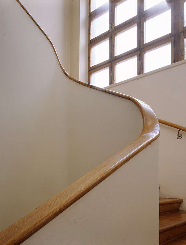 White stairway with a curved wooden railing and lattice