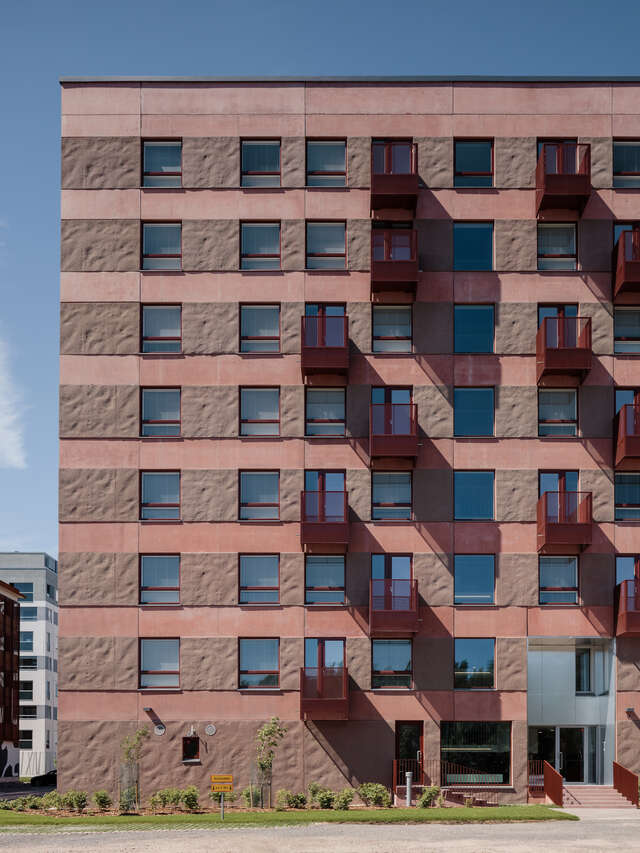 A wall of a red apartment building with windows and scattered balconies.