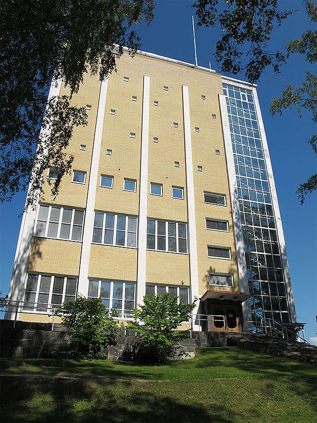 Tall yellow brick building with a glass wall stairway on the right edge of the building.