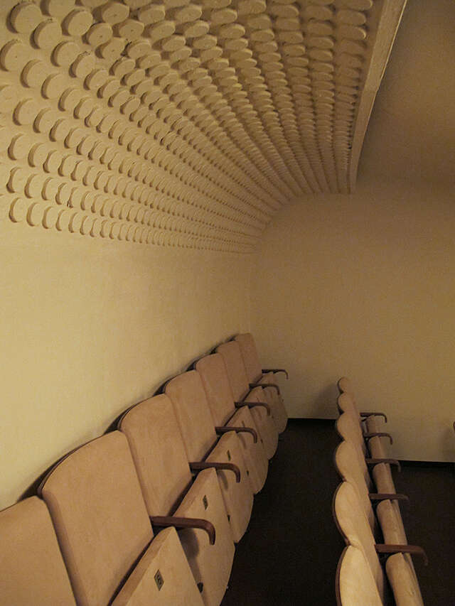 Beige movie seat rows in a cream colored room with a rounded ceiling edge with small disks in it.