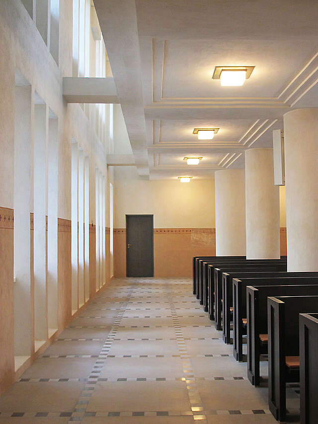 Hallway next to the church benches, terra-cotta colored paint covers half of the wall.