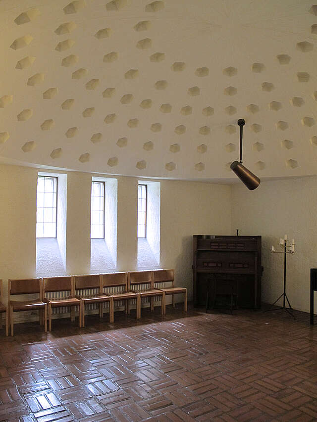 Light chapel interior with a Rome ceiling and wooden seats on the side.