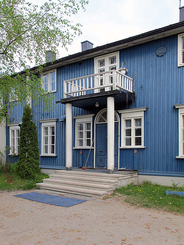 Old blue wooden house with white window frames and balcony.
