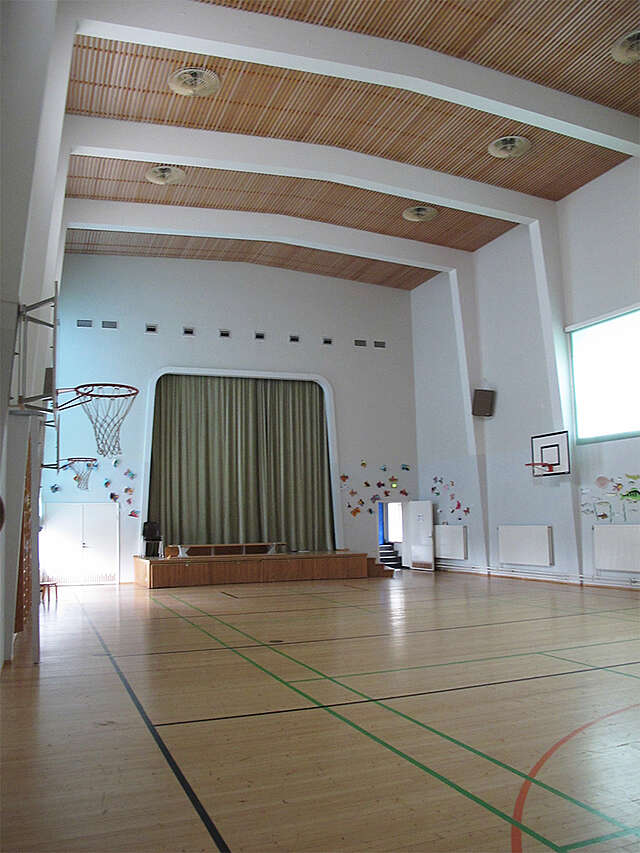 school gymnasium with basketball bakers, colored lines on the floor and a stage with curtains at the back.