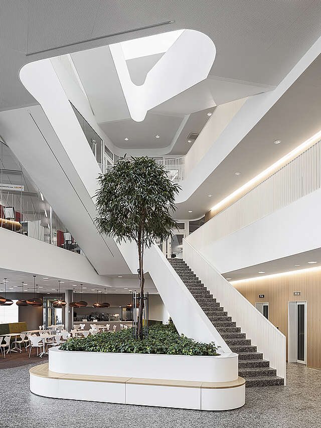 Stone staircase with white railings connecting every floor and with a ceiling window on top.