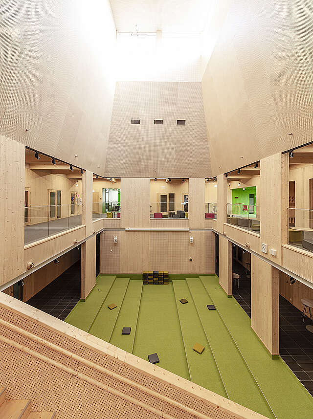School hall with wooden surfaces and a green sitting area in the middle of the building.