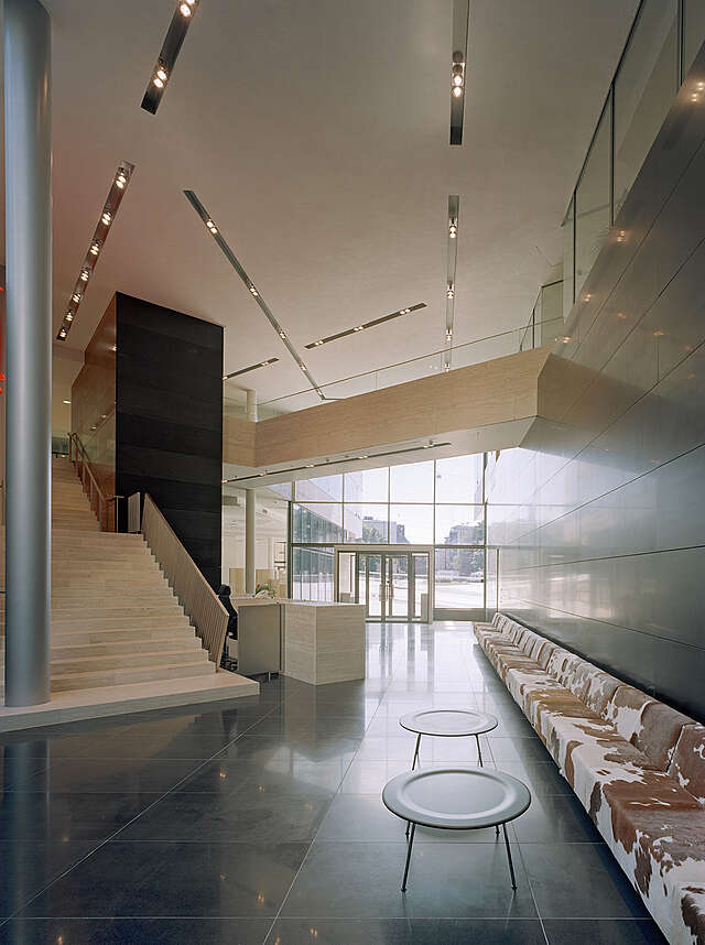 View of the entrance hall with a leather bench on the left, glass doors at the back and stairs at the right.