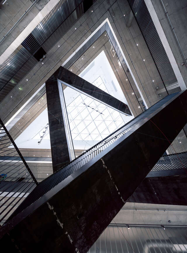 Image looking up through several floors. Staircases interloping diagonally and large glass skylight at very top.