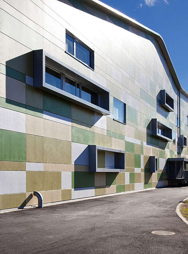 Different-sized cement composite panels in white and shades of green are used to create a vivid and playful patchwork. The facades are punctuated by protruding aluminium-framed windows.