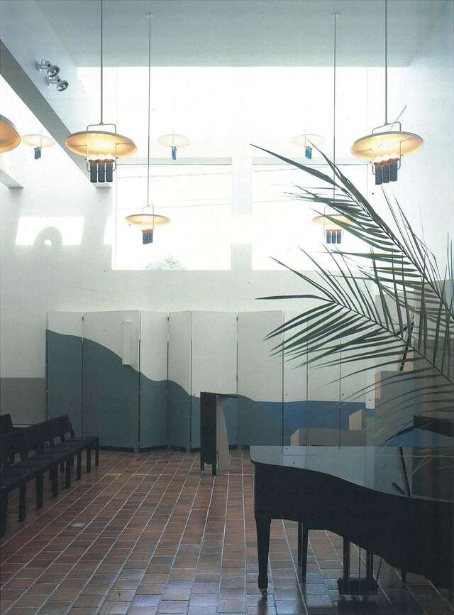 Large parish hall with chairs, flygel and an indoor plant.