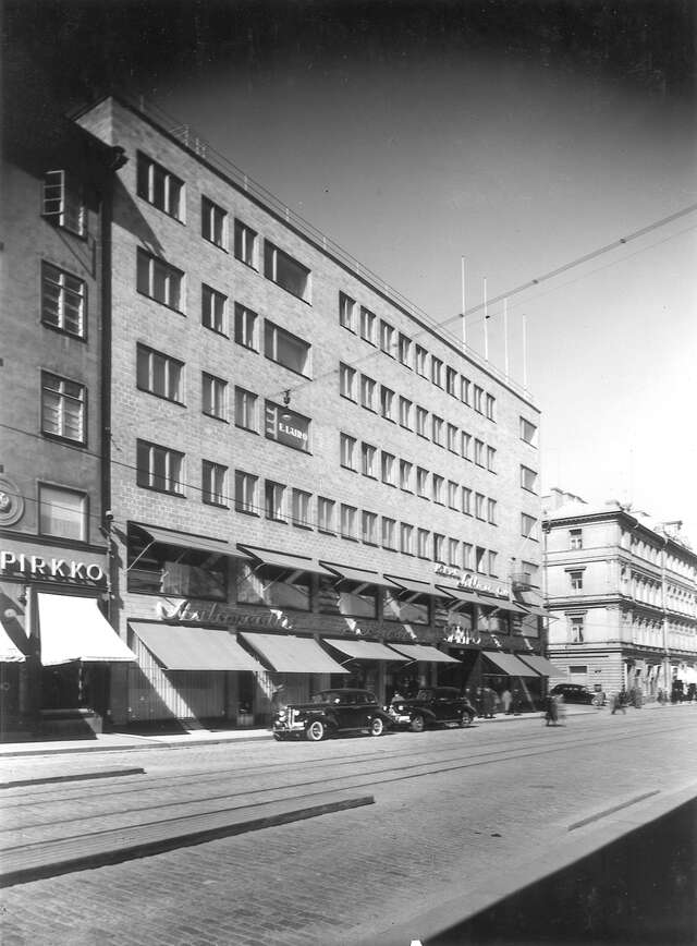 Black and white image of a brick building in front of tram tracks.