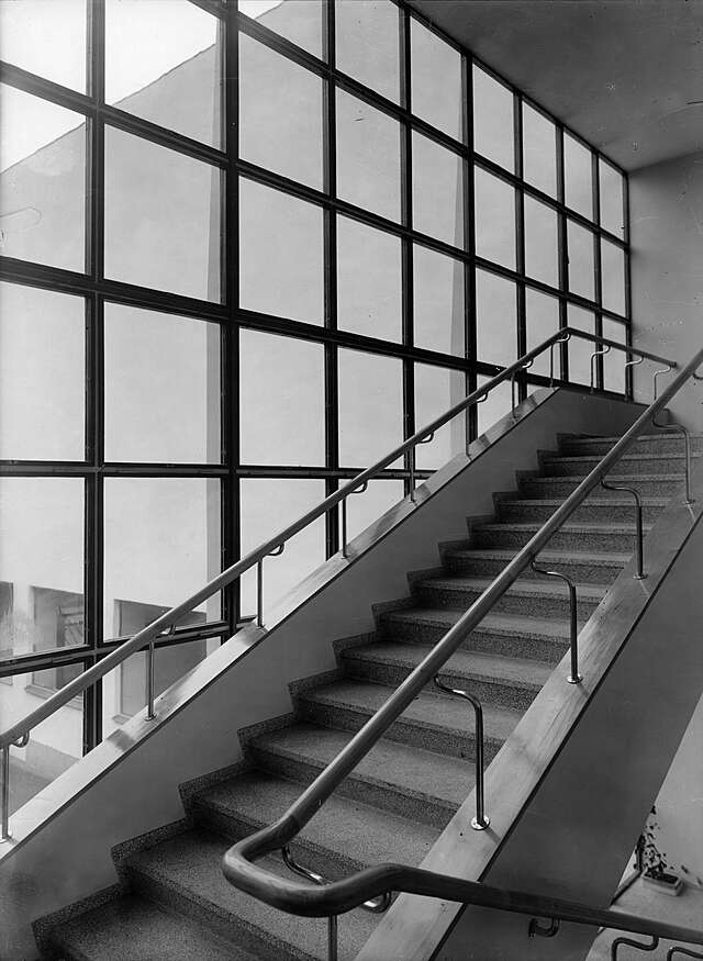 Stairs with stone, white and metal elements next to a glass wall.
