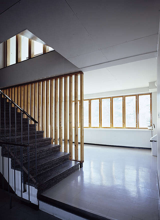 Stairway leading left up, open wooden dividing wall and window ribbon on the right
