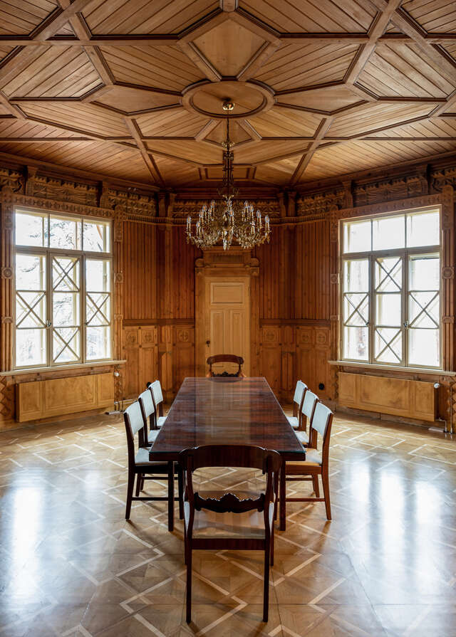 Dark wood panel walls and ceiling with decorations, diagonally a dark wooden dining table