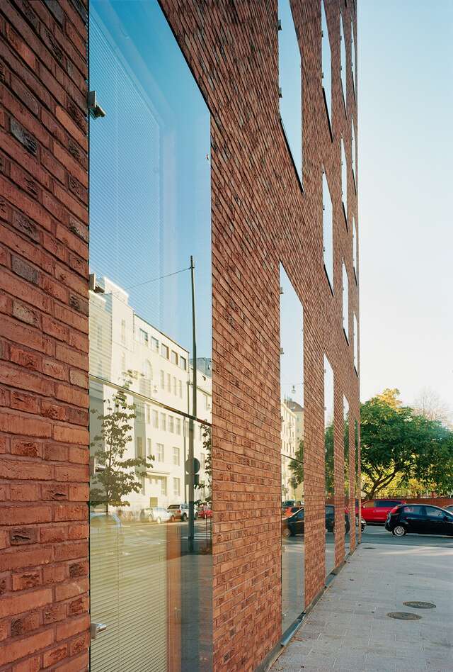 Façade detail with red brick elements and glazing mirroring the opposite white building