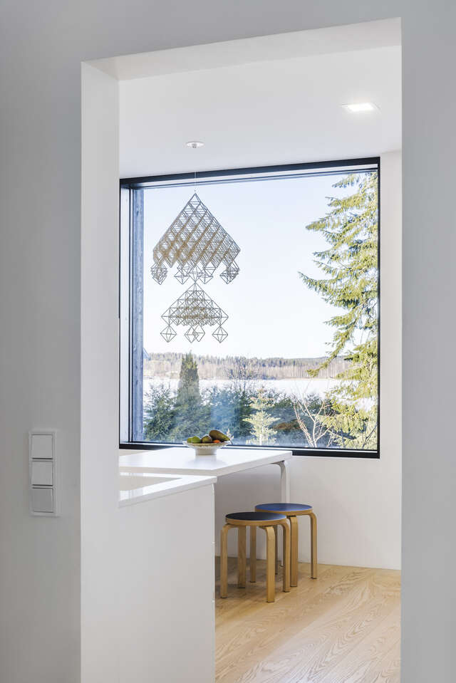 A large, square window shows a view outside. a table with two stools is in front of the window.