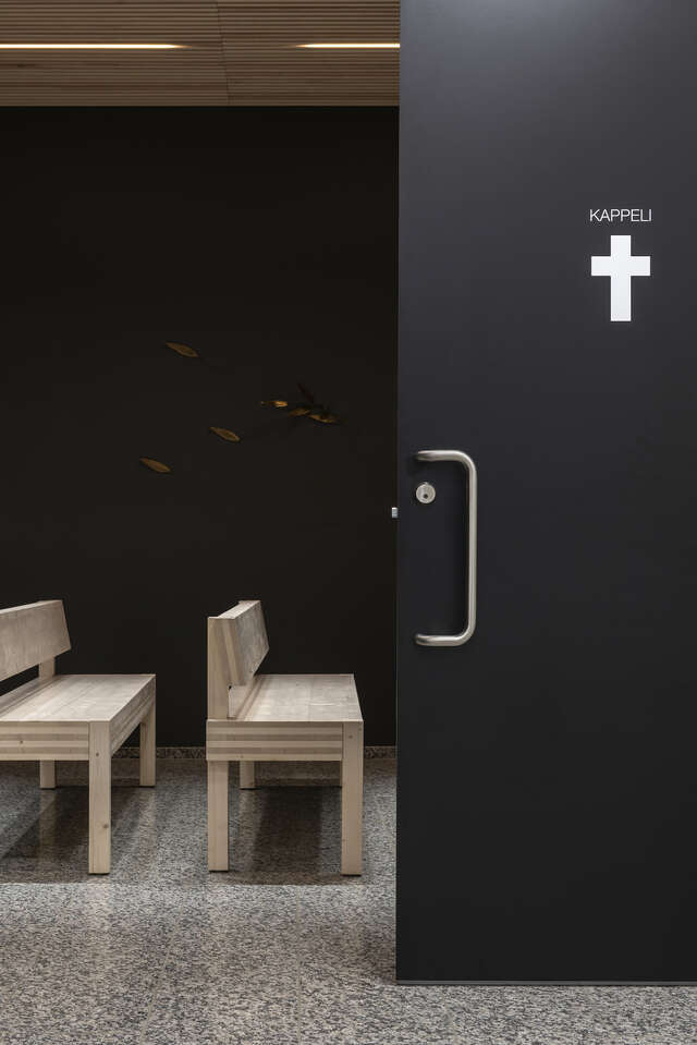 A black door with a cross on it is slightly open, revealing church pews.