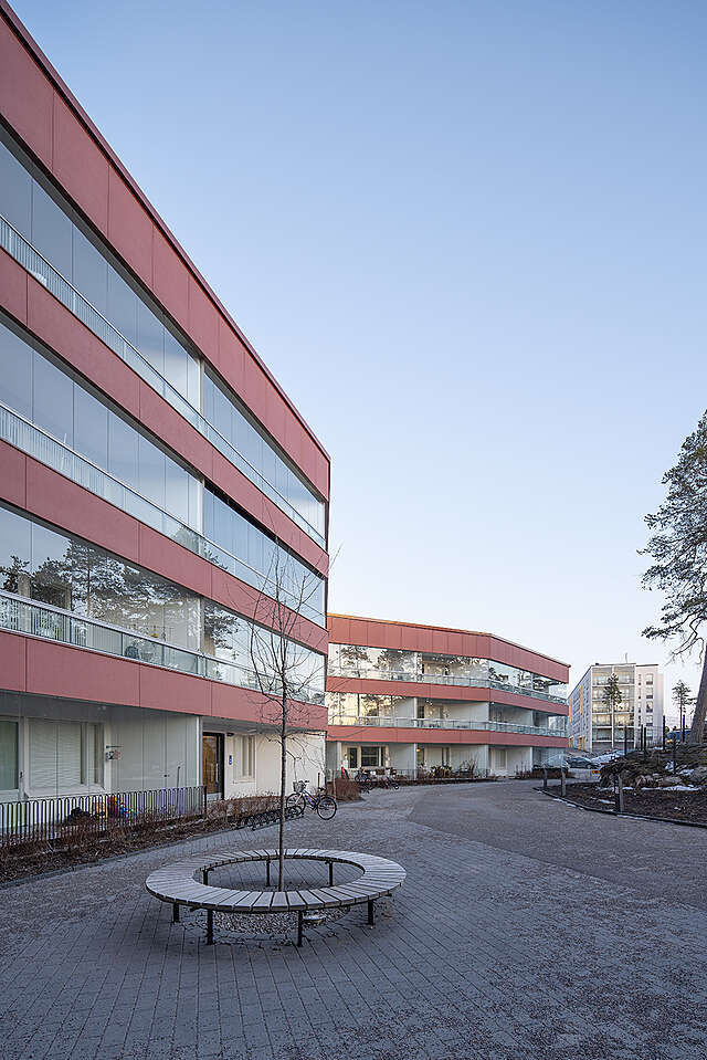 Four storey apartment building with several wings and red metal panels on each floor.