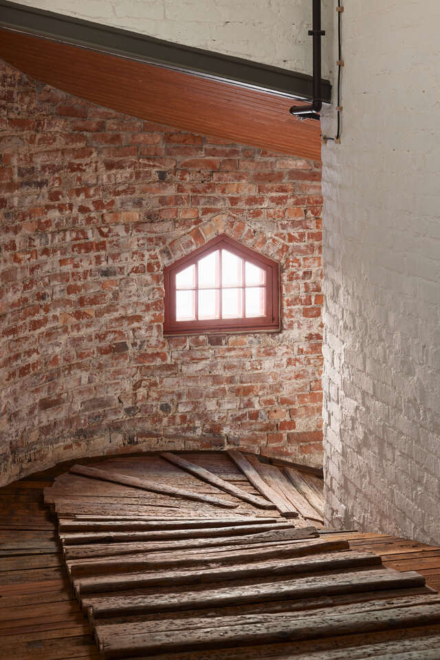 Wooden steps winding down in a brick-walled stairway with a small window.