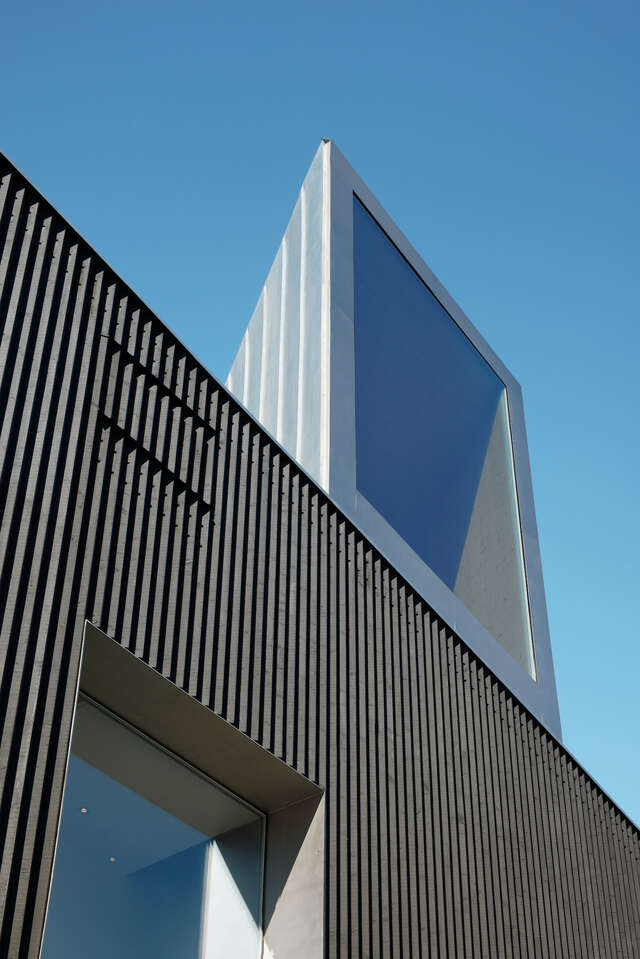 Wooden black exterior wall with large window above it.
