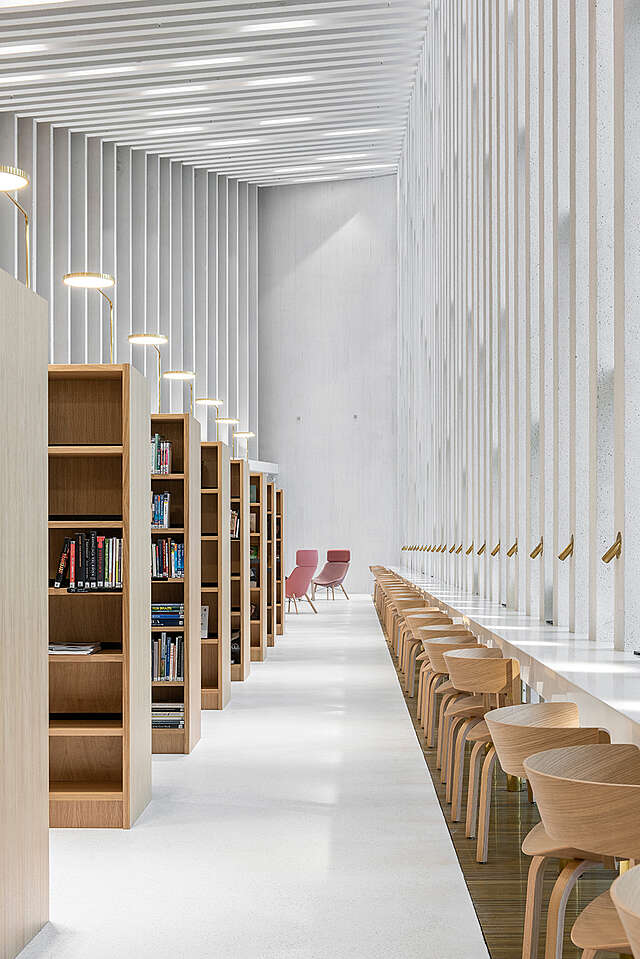 White tall space, desks and chairs in front of windows, wooden bookshelves