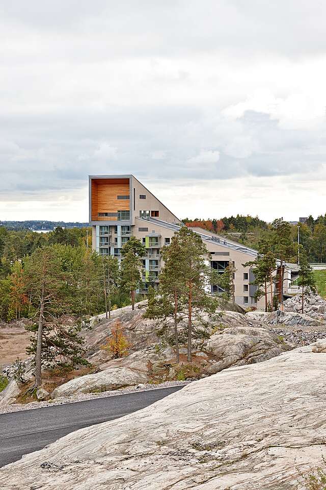 Multiple story residential building with a slanted roof, a balcony at the highest level and a view of the forest.