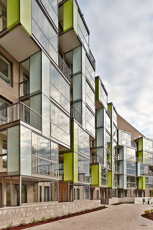 Multiple story residential building with protruding balconies with colored green and blue glass details.