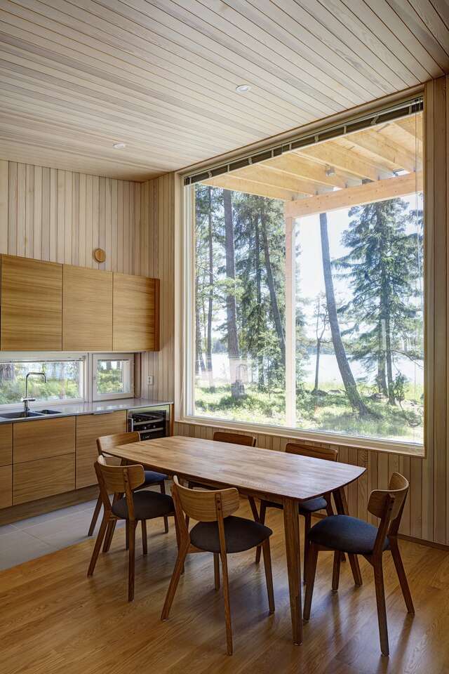 A kitchen with a large window looking outside has a wooden table and six chairs in front of it.