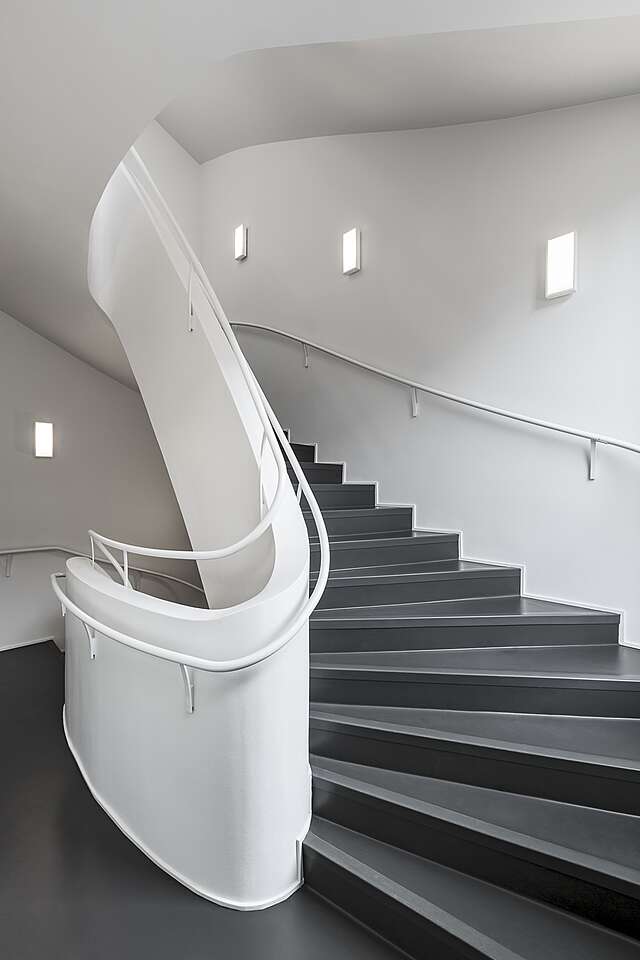 White curved staircase with grey stairs and small white lights on the wall.