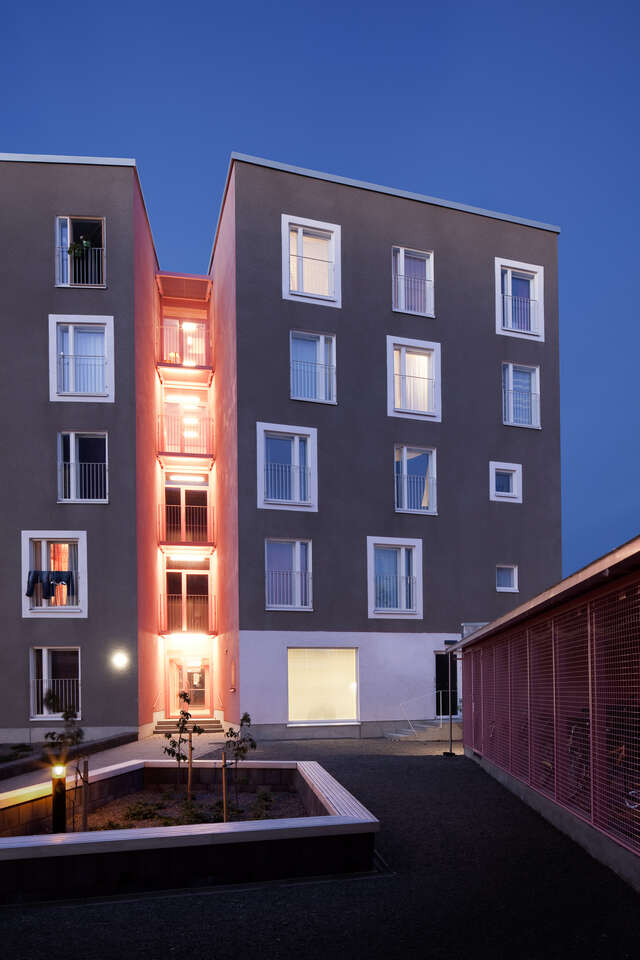 End of grey five-storey block house with a lower entrance part and a courtyard