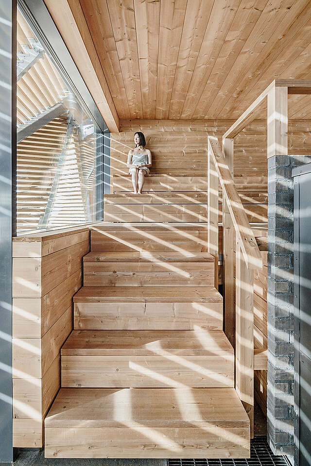 Woman sitting in a sauna with a large glass window.