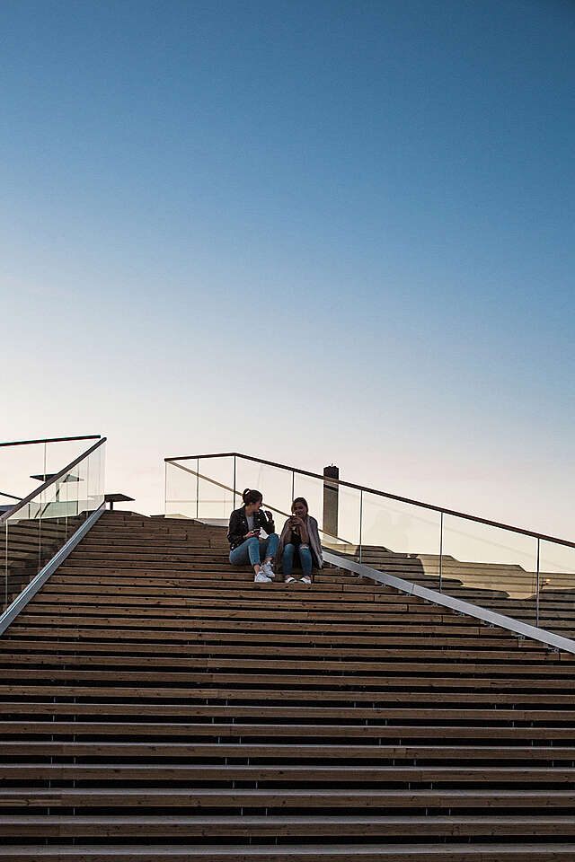 Two young women sitting on the löyly stairs during sunset.