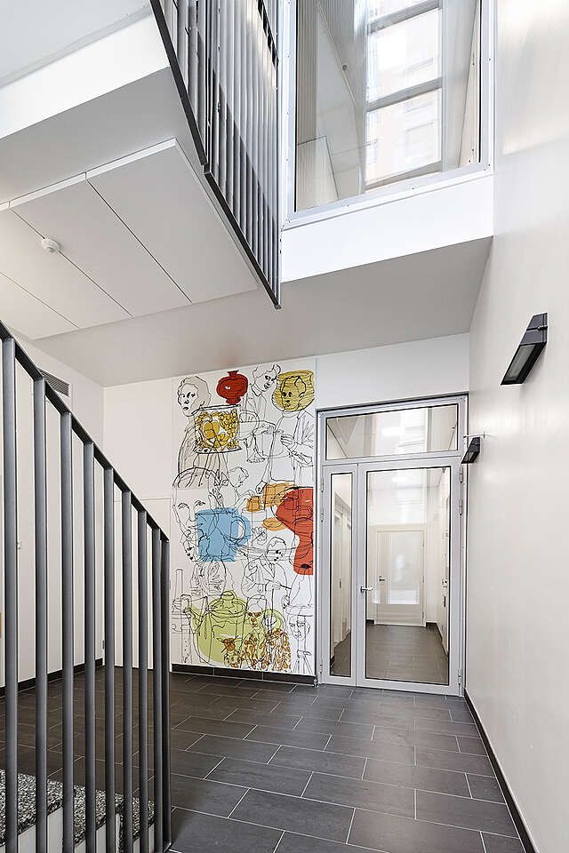 Large art piece in a stairway, depicting people and household items.