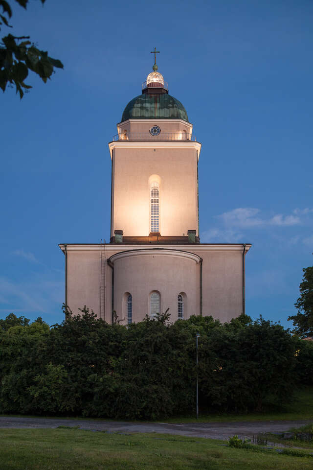 Frontal perspective of the light-coloured stone church and lighthouse with a patina dome