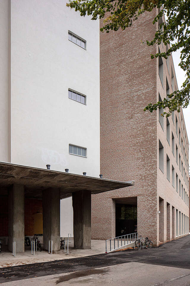 Large stone structure seen from outside. White building on the left and brown building on the right.